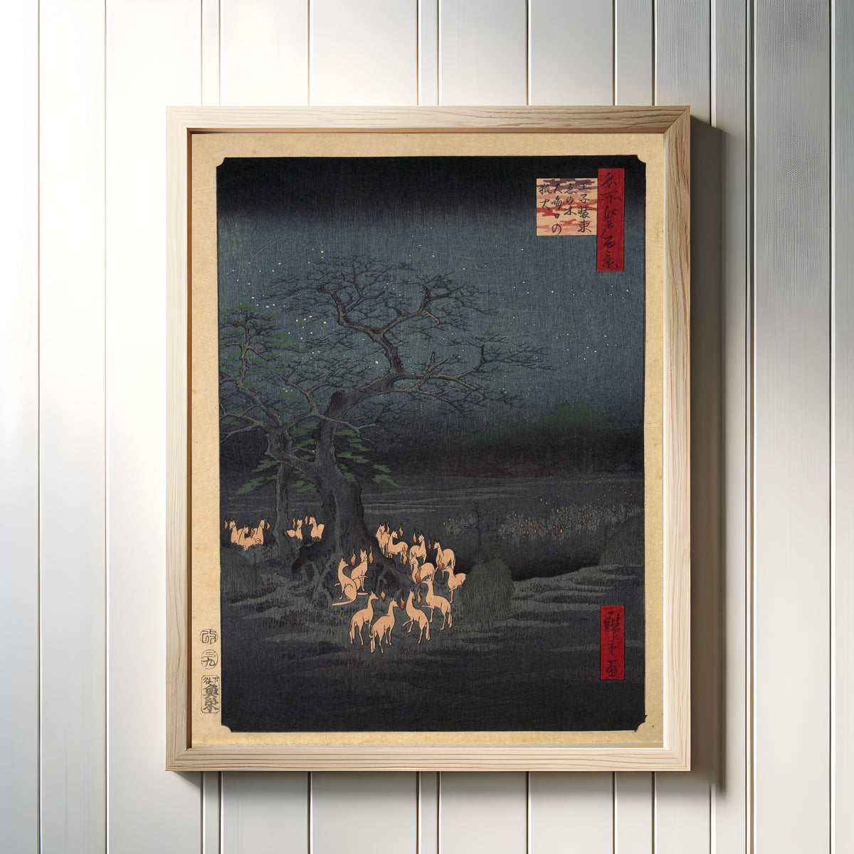Framed art print of New Year's Eve Foxfire by Utagawa Hiroshige, in a light wood frame on a white panelled wall