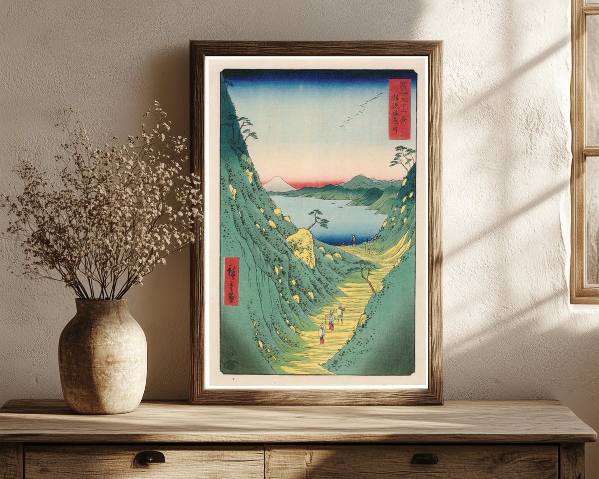 Framed art print of Shiojiri Pass in Shinano Province by Utagawa Hiroshige, in a dark wood frame leaning on a rustic console beside dried flowers