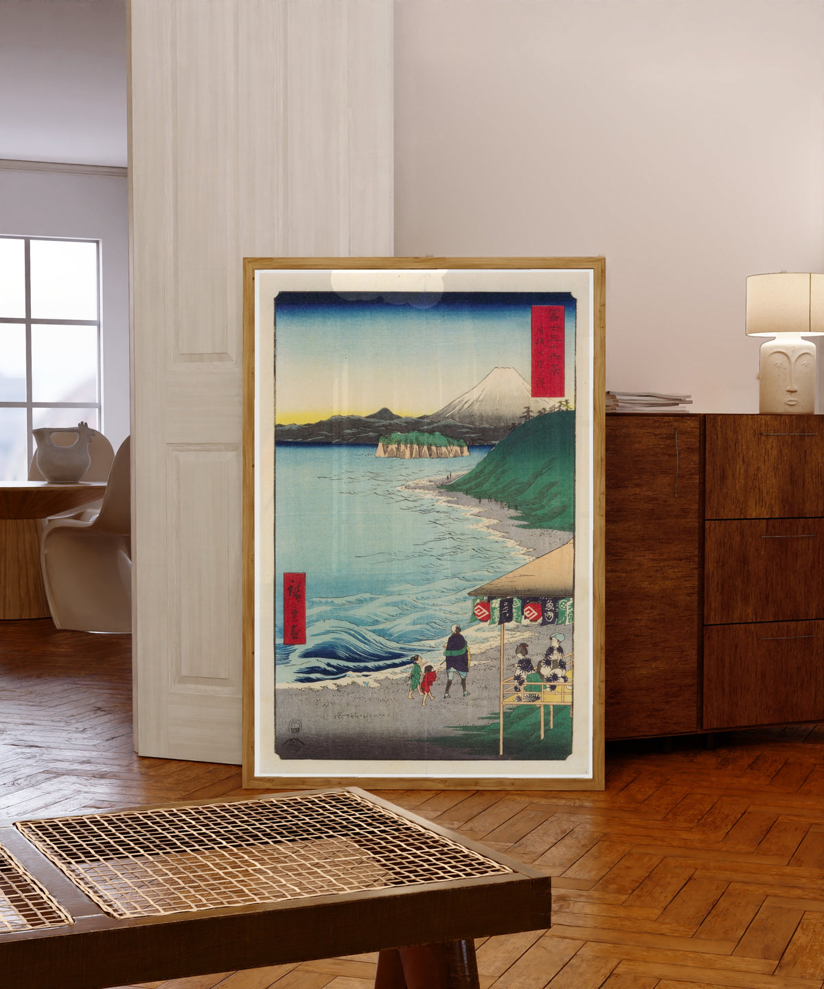 Framed art print of The Seven Ri Beach in Sagami Province by Utagawa Hiroshige, in a light wood frame leaning in a warm room with a parquet floor