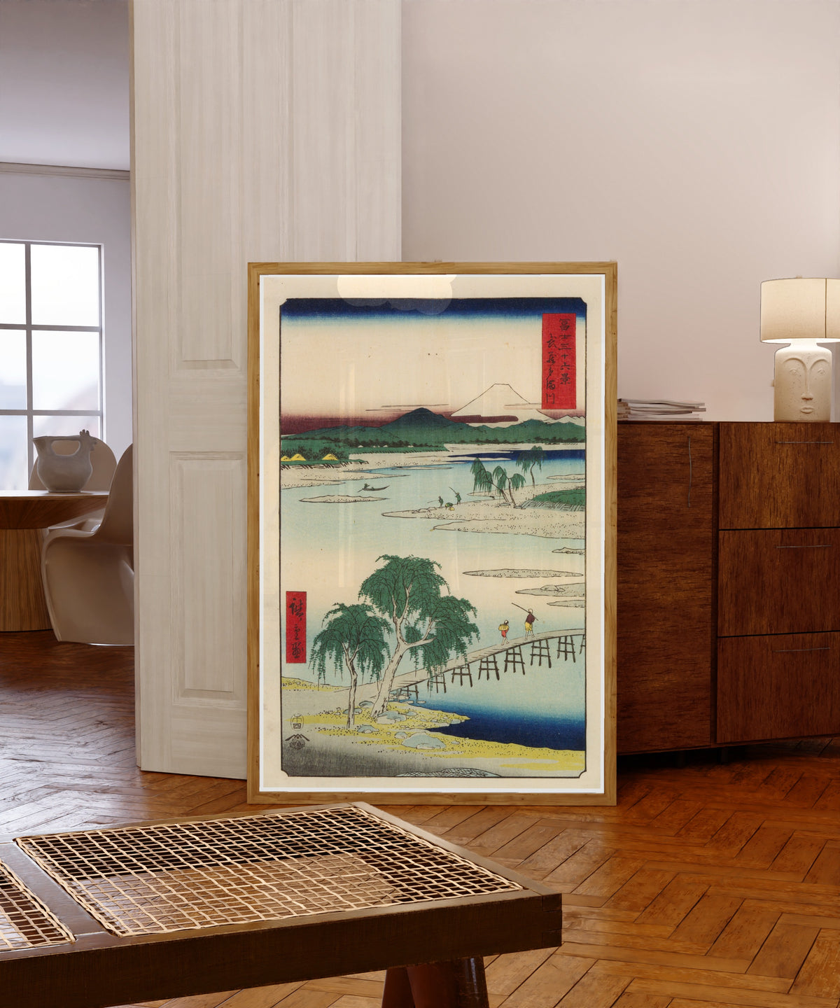 Framed art print of The Tama River in Musashi Province by Utagawa Hiroshige, in a light wood frame leaning in a warm room with a parquet floor
