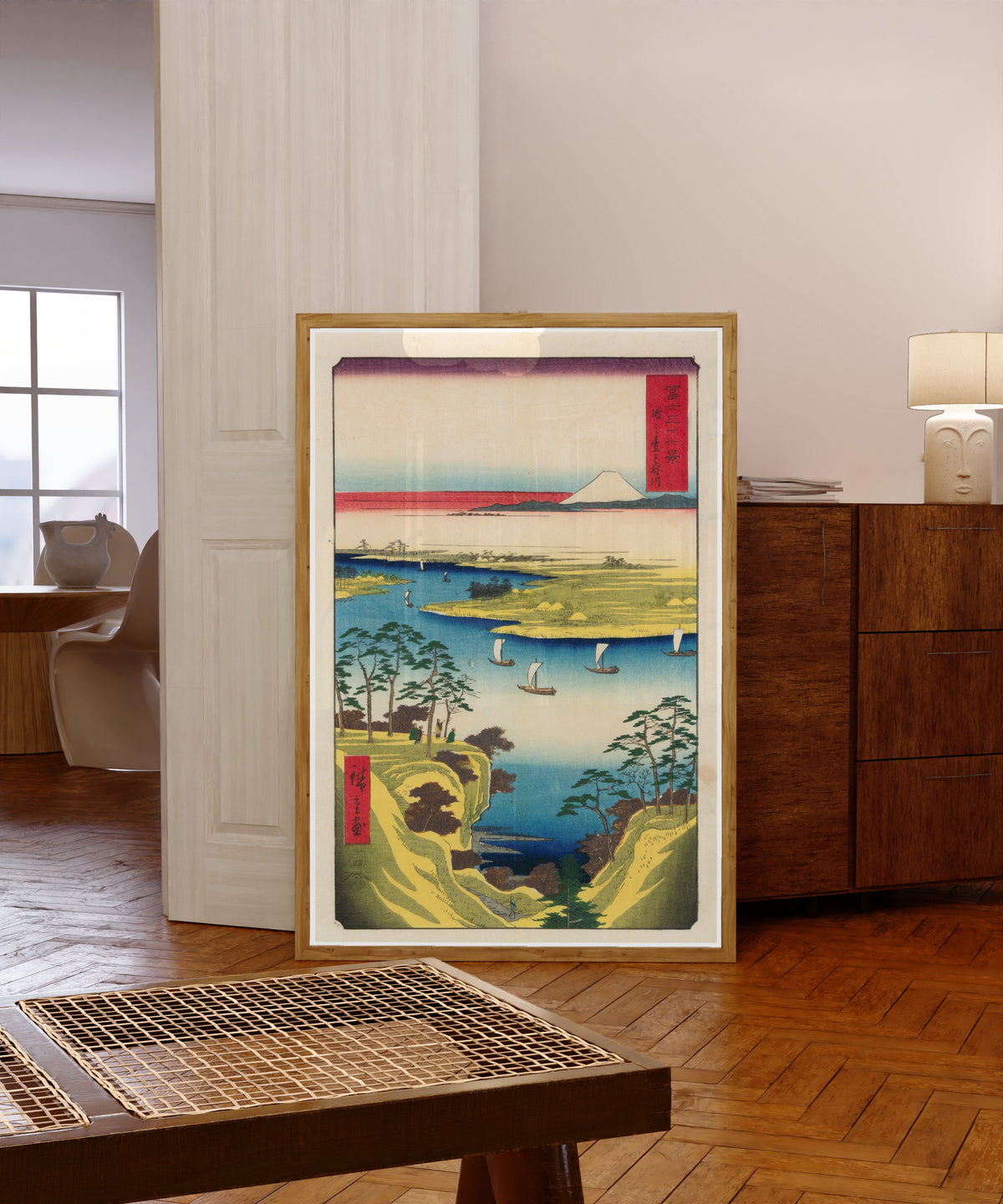 Framed art print of Wild Goose Hill and the Tone River by Utagawa Hiroshige, in a light wood frame leaning in a warm room with a parquet floor