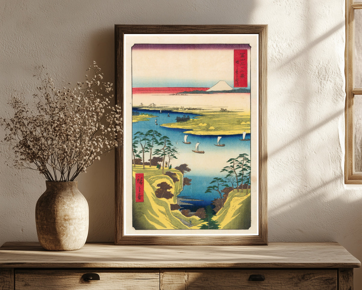 Framed art print of Wild Goose Hill and the Tone River by Utagawa Hiroshige, in a dark wood frame leaning on a rustic console beside dried flowers