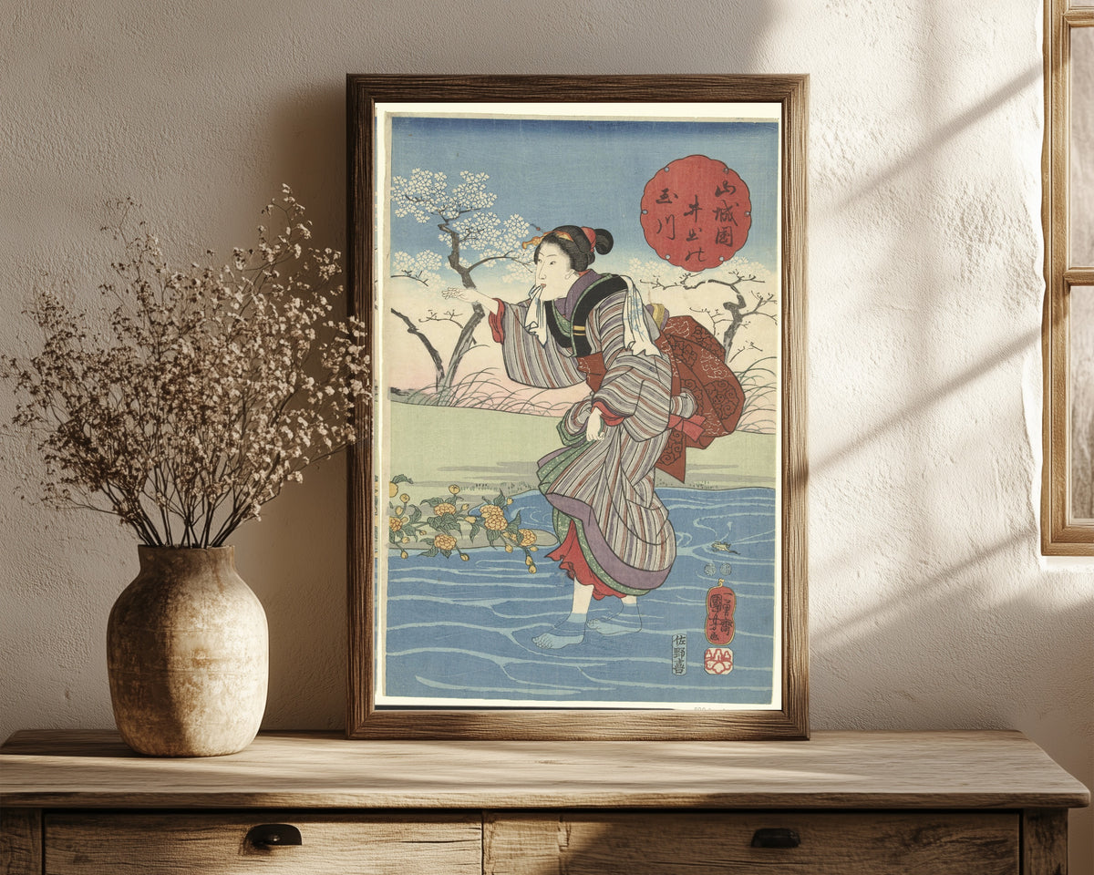 Framed art print of The Ide Tama River in Yamashiro Province by Utagawa Kuniyoshi, in a dark wood frame leaning on a rustic console beside dried flowers
