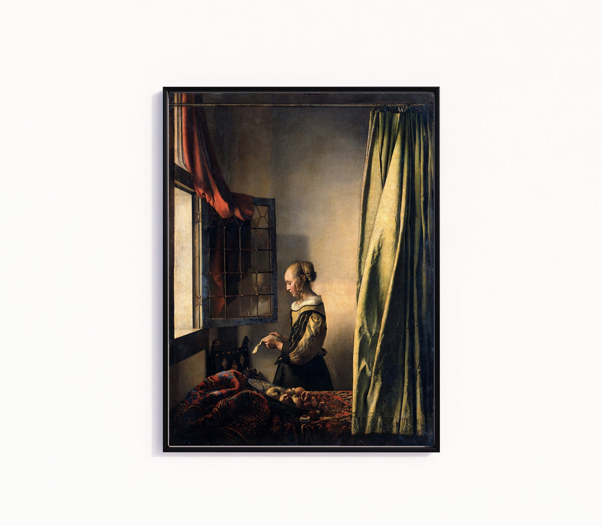 Framed art print of Young Woman Reading a Letter at an Open Window by Johannes Vermeer, in a slim black frame on a plain white wall