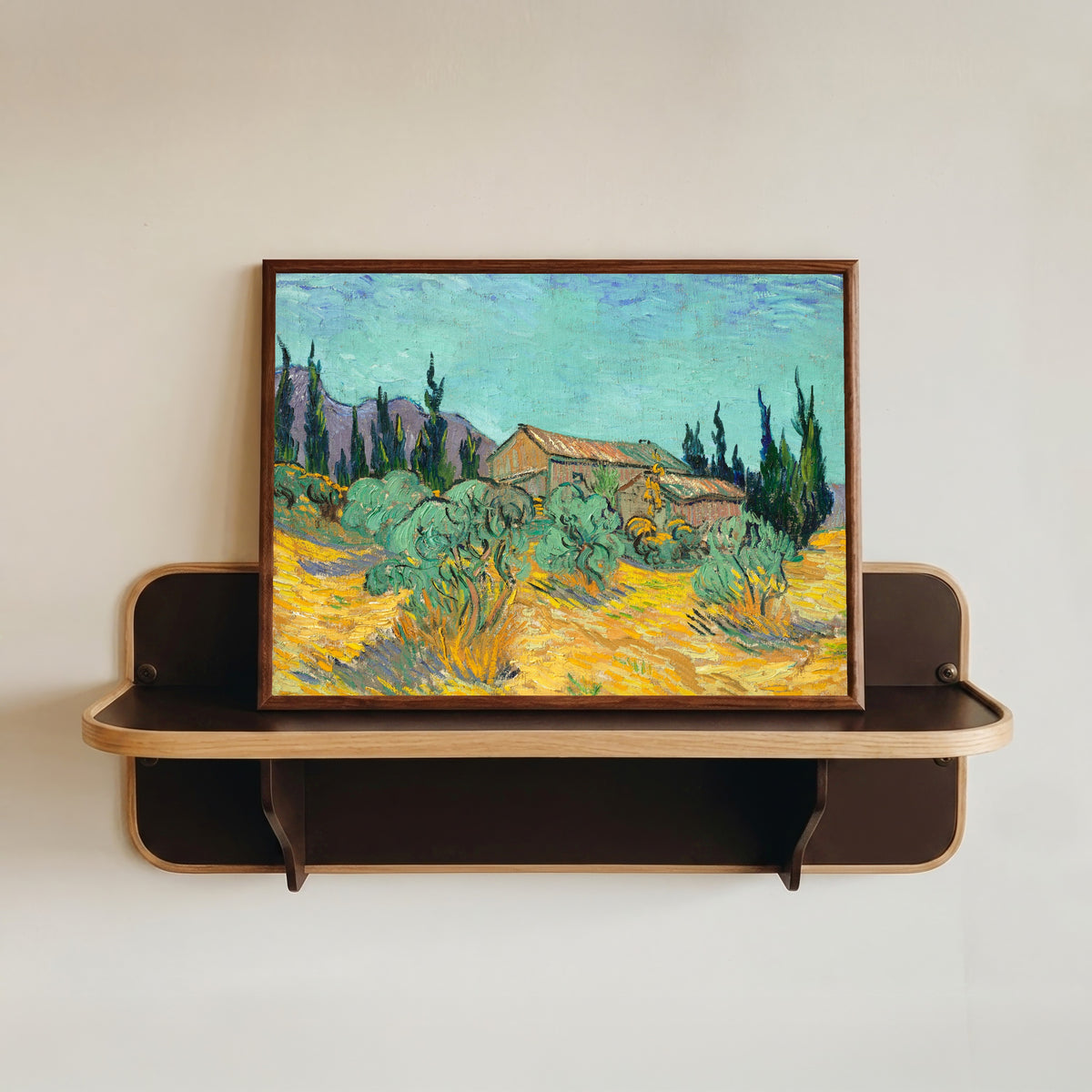 Framed art print of Huts surrounded by Olive Trees and Cypresses by Vincent van Gogh, in a dark wood frame resting on a wall shelf