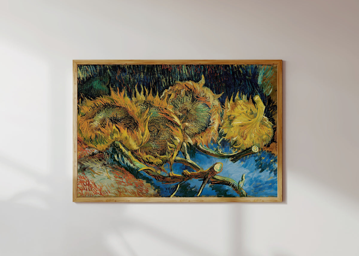 Framed art print of Sunflowers by Vincent van Gogh, in a light wood frame on a sunlit white wall