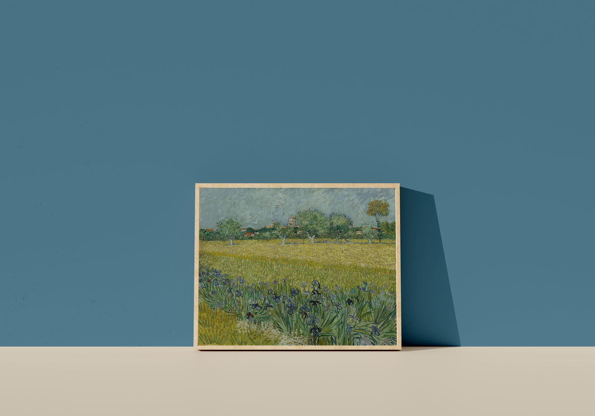 Framed art print of View of Arles with Irises by Vincent van Gogh, in a light wood frame leaning on a blue wall