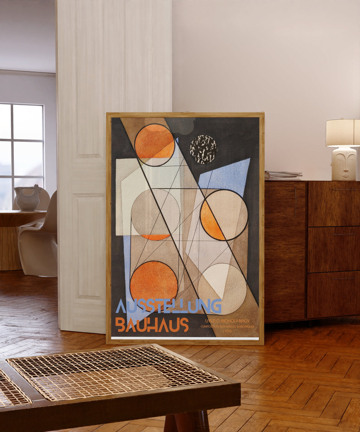 Framed art print of Composition aux Cercles Symétriques by László Moholy-Nagy, in a light wood frame leaning in a warm room with a parquet floor