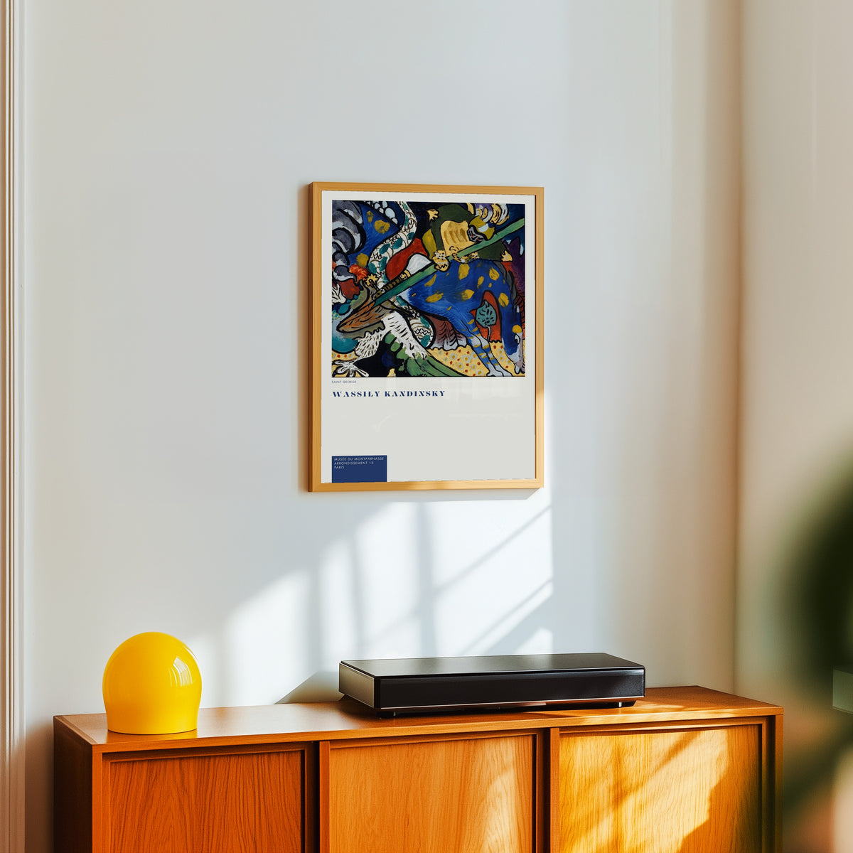 Framed art print of St. George by Wassily Kandinsky, in a light wood frame on a white wall above an orange sideboard