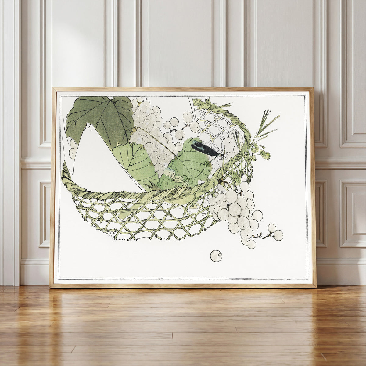 Framed art print of Basket of grapes from Seitei Kacho Gafu (1890–1891) by Watanabe Seitei, in a light wood frame leaning against a panelled white wall