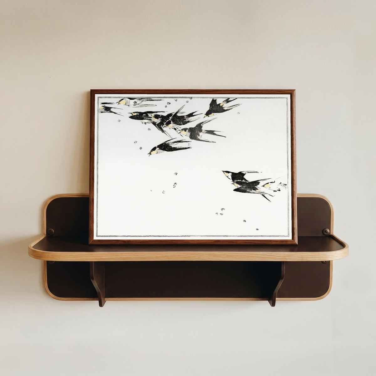 Framed art print of Swallows in Flight by Watanabe Seitei, in a dark wood frame resting on a wall shelf