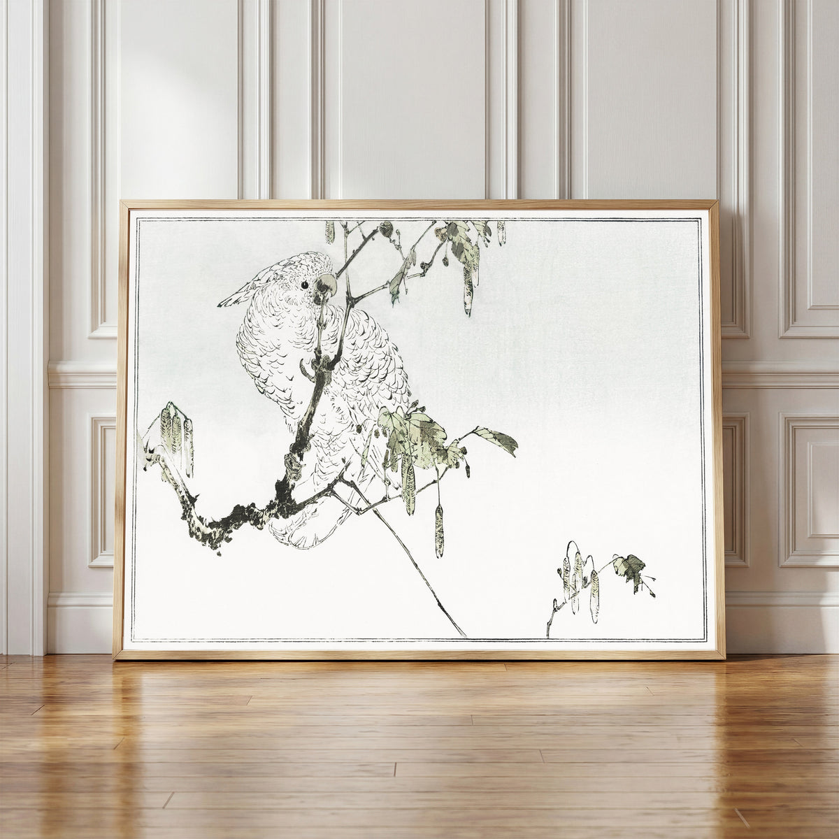Framed art print of White cockatoo perched on a branch by Watanabe Seitei, in a light wood frame leaning against a panelled white wall