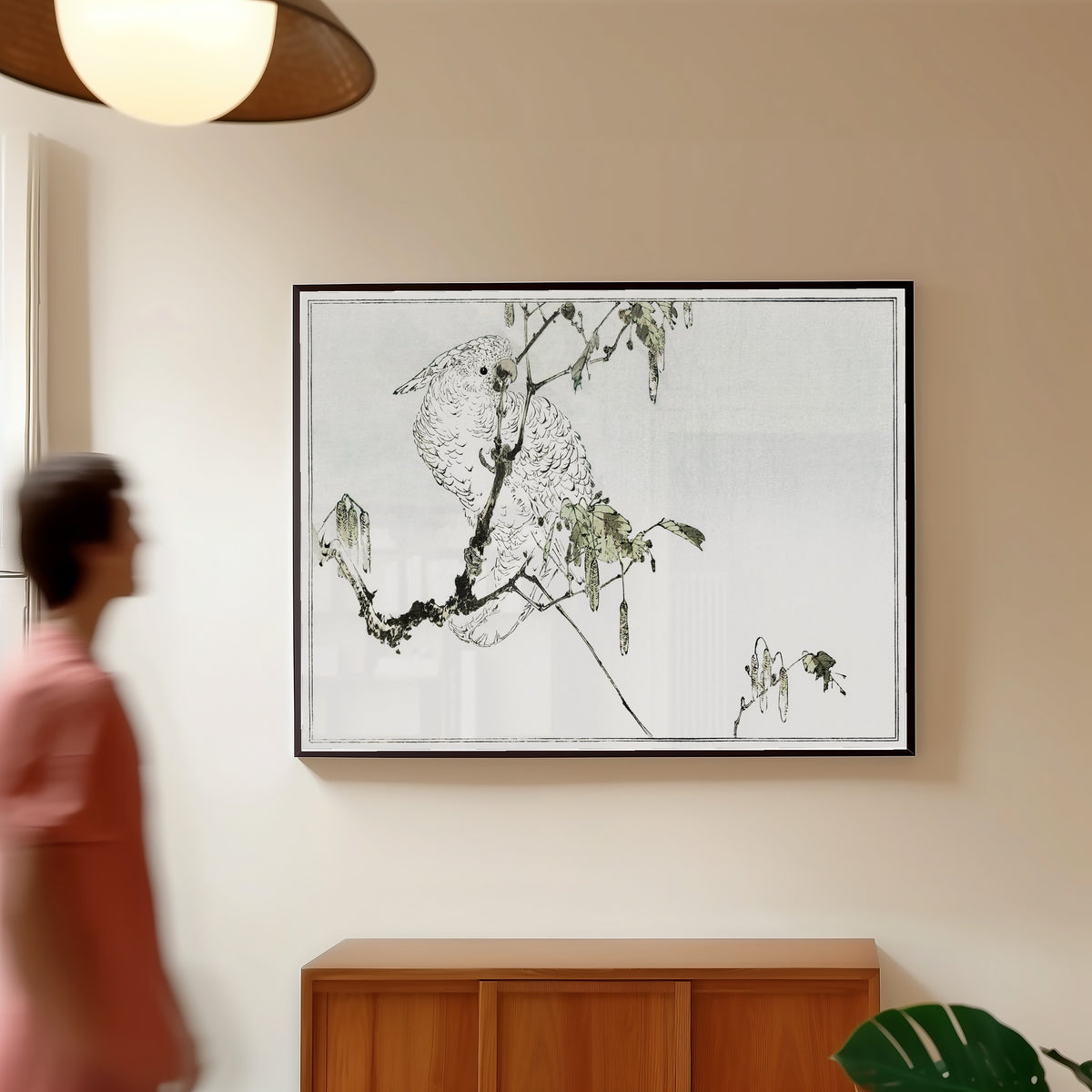Framed art print of White cockatoo perched on a branch by Watanabe Seitei, in a slim black frame on a warm wall in a sunlit room