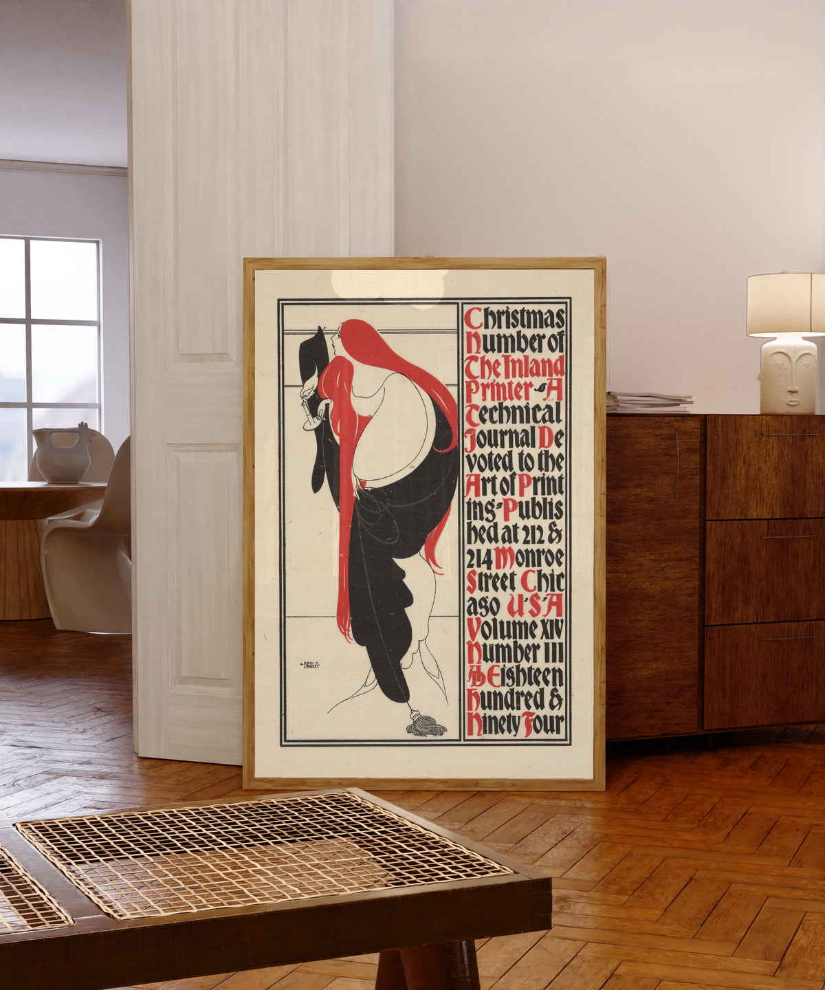 Framed art print of The Inland Printer, Christmas Number, 1894 by Will Bradley, in a light wood frame leaning in a warm room with a parquet floor